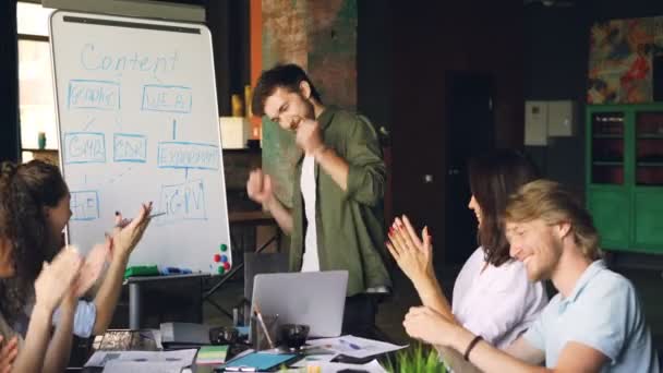 Handsome guy trainer is finishing presentation and rejoicing laughing, dancing and bowing while audience is applauding and doing high five. Successful work and people concept. — Stock Video