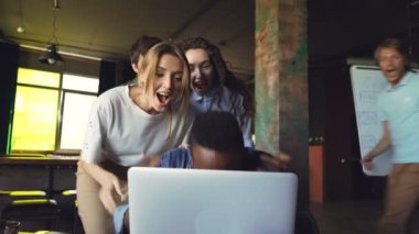 Afrika kökenli Amerikalı adam ofis çalışanı iyi haber hakkında heyecanlı, dizüstü bilgisayar ekranına bakarak ve gülüyor, ekibi başarı kutluyor, eller alkışlar ve onu tebrik.