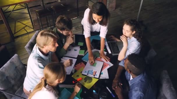 Vue en grand angle des jeunes collègues discutant de graphiques, puis mettant la main ensemble et les élevant exprimant l'esprit d'équipe assis au bureau dans un bureau moderne .