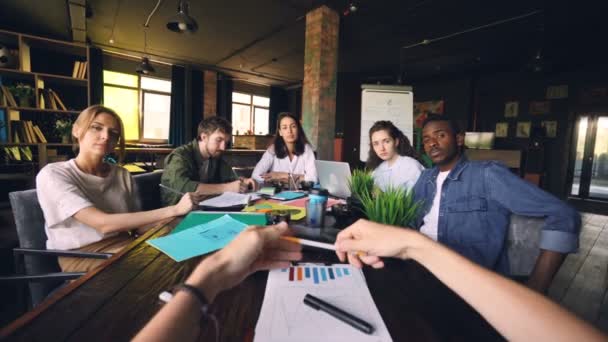 Company owner is talking to his employees at meeting sitting at table while group of young people is looking at him and listening to him. Management and business concept. — Stock Video