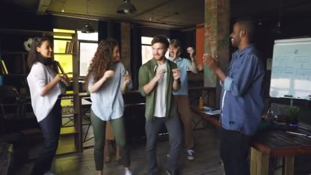 Radostné kolegy zaměstnance mezinárodní společnosti se tančí na firemní oslavě slaví svátek směje a tleská rukama. Moderní loft stylu office je v pozadí.