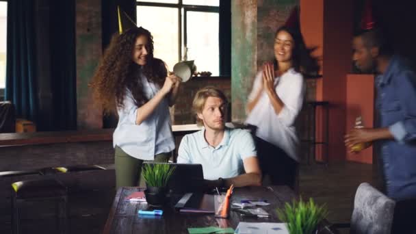 Les employés de l'entreprise félicitent leur patron pour leur anniversaire en apportant du gâteau et des chapeaux de fête, jeune homme souffle des bougies et fait cinq hauts pendant que les travailleurs applaudissent les mains . — Video