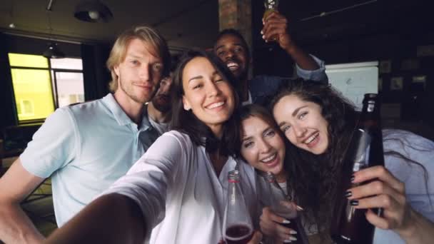 Retrato en cámara lenta de un grupo de compañeros de trabajo tomando selfie con bebidas en la fiesta de la oficina, hombres y mujeres atractivos posando con caras divertidas, sosteniendo botellas y riendo . — Vídeos de Stock