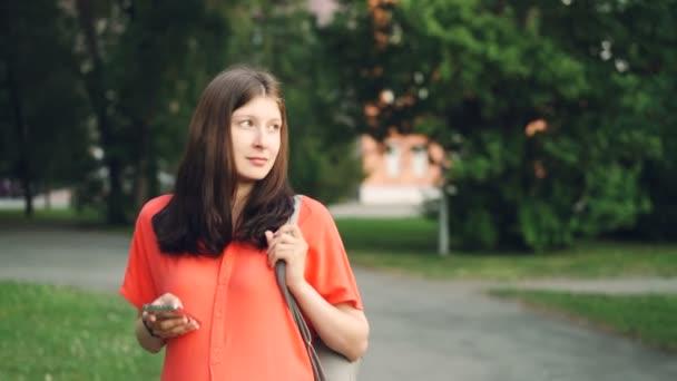 Jolie femme enceinte utilise un smartphone regardant l'écran marcher dans le parc le jour de l'été. Technologie moderne, mode de vie sain et concept de grossesse . — Video