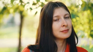 Yakın çekim portre gülümseyen ve rüzgarlı ve güneşli gün Park kamera ayakta bakarak çekici genç hanım. Sağlıklı yaşam, güzel doğası ve gençlik kavramı.