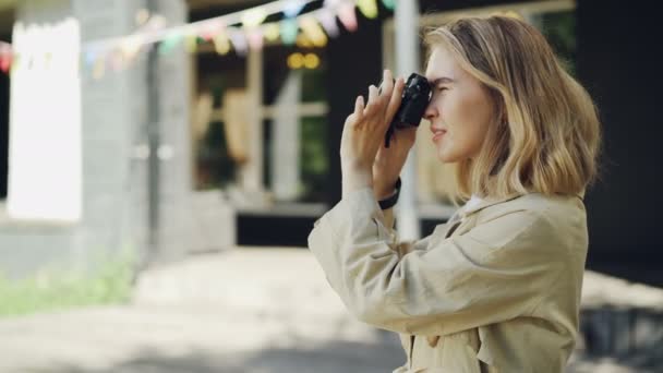 Attraktiv ung kvinna fotograf tar bilder med moderna kameran stående utomhus i vackra staden sommardag. Människor, hobby och livsstil koncept. — Stockvideo