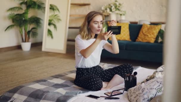 Belle fille utilise des cosmétiques pour peindre les sourcils, elle tient le pinceau et applique du maquillage en regardant le miroir. Concept beauté, personnes et appartements . — Video