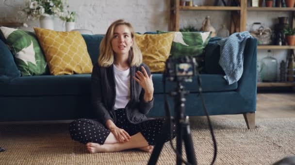 Mujer joven creativa está grabando vídeo para sus suscriptores para videolog de Internet, ella está mirando a la cámara en el trípode y hablando. Concepto de redes sociales y personas . — Vídeo de stock