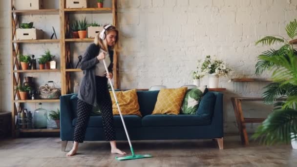 Ragazza creativa sta cantando e ballando con lo straccio durante i lavori domestici in bella casa con bei mobili e piante. Divertimento, lavoro domestico e concetto di persone felici . — Video Stock