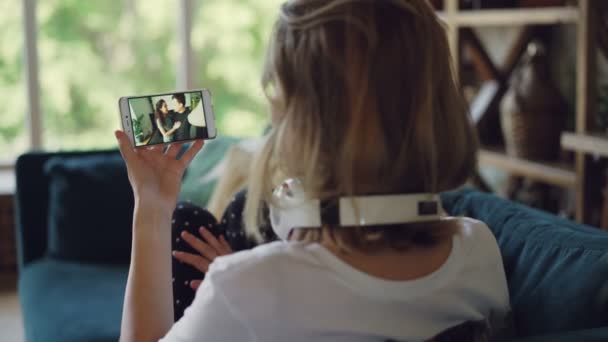 Blond dziewczyna robi połączenie wideo smartfonem, rozmawiając z przyjaciółmi, patrząc na ekran i ciesząc się nowoczesnej komunikacji. Koncepcja technologii, ludzi i domu. — Wideo stockowe