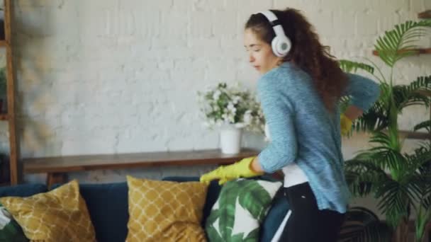 Bonita joven ama de casa está lavando el piso en el apartamento de estilo loft y escuchando música en los auriculares, ella está cantando y bailando divirtiéndose con fregona. — Vídeos de Stock