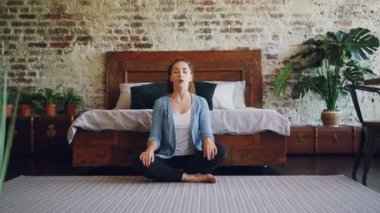 Genç kadın ev diz elleriyle lotus poz dinlenme ve nefes yoga pratik. Meditasyon, sağlıklı yaşam tarzı ve modern yatak odası konsepti.