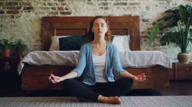 Güzel genç bayan lotus bulunduğu yatak odasının zemininde ve meditasyon, uyum ve zevk barış üzerinde oturuyor. Modern evler, sağlıklı insanlar ve dinlenme kavramı.