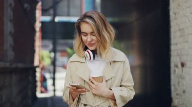 Oldukça genç bayanın ekran dokunaklı ve açık havada gitmek kahve içme smartphone tutarak yavaş. Kentsel yaşam tarzı, take away içecekler ve modern teknoloji kavramı.
