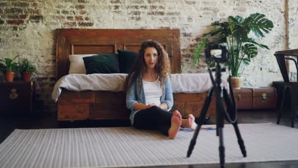 Attraktiv ung kvinna med långt lockigt hår blogger är videoinspelning för sin internetblogg med kamera, flicka är visar smartphone och fotografier och talar. — Stockvideo