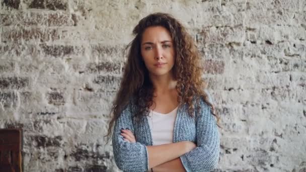 Retrato de una chica infeliz mirando a la cámara, frunciendo el ceño y sacudiendo la cabeza de pie con los brazos cruzados con la pared de ladrillo en el fondo. Concepto de emociones, sentimientos y personas . — Vídeos de Stock