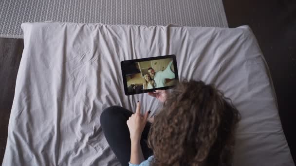 Молода леді розмовляє з красивою парою онлайн з планшетом, дивлячись на екран і розмовляючи сидячи на ліжку вдома. Сучасні технології, розмова та концепція молоді . — стокове відео