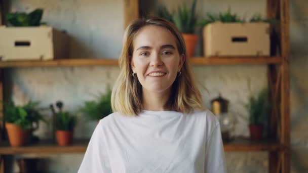Zpomalený pohyb portrét veselá dívka s plavými vlasy při pohledu kamery, usmívá a směje se stojící interiéru v moderním bytě. Mladí lidé a pozitivní emoce koncepce. — Stock video