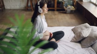 Güzel hamile kadının karnı modern daire yatakta oturup ve kulaklıklar giyen müzik okşayarak. Gebelik, iç ve mutluluk kavramı.