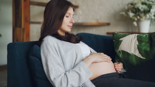 Bella giovane donna in attesa di madre sta accarezzando la pancia e guardandola esprimere l'amore per il nascituro. Famiglia giovane, genitori amorevoli e concetto di maternità . — Video Stock