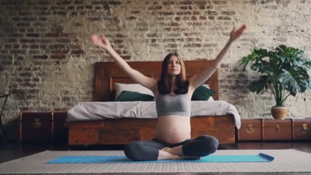 Sportif hamile kadın yoga mat eller yükselterek, palms araya koyarak sonra rahatlatıcı yatak odasının zemininde ve lotus pozisyonda breating evde oturan, pratik. — Stok video
