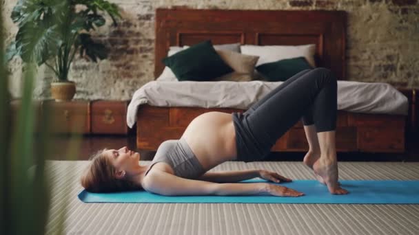 Sportief zwanger meisje is het beoefenen van fitness oefeningen op lichte yoga mat in moderne loft stijl slaapkamer. Gezonde levensstijl, mensen en zwangerschap concept. — Stockvideo