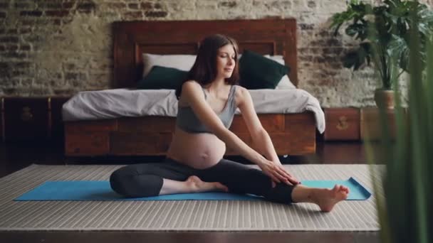 Красивая брюнетка ожидает мать делает упражнения растяжения наклон вперед к ноге практикуя йогу для будущих матерей и наслаждаясь деятельности дома . — стоковое видео