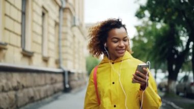 Kaygısız Afro-Amerikan öğrenci yürüyüş, kulaklık üzerinden müzik ve serbest zaman sırasında şarkı. Modern teknoloji, gençlik kültürü, şehirler ve insanlar kavramı.
