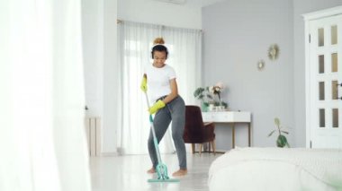Oldukça karışık yarış kız neşeli hizmetçi güzel düz zeminde plastik paspas ile temizlik ve şarkı ve dans müzik dinleme. Rutin ve eğlenceli kavramı.