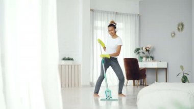 Komik Afrikalı-Amerikalı genç ev temizliği bez ve kulaklık müzik dinlemek zemin temizlik ev işi yapıyor, kız dans şarkı ve.