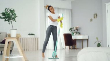 Yakışıklı Afro-Amerikan ev kadını temizlemenizi ve having fun paspas ve kulaklık müzik keyfi şarkı etrafında dans. İnsanlar ve sevinç kavramı.