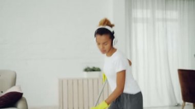 Güzel Afrikalı-Amerikalı genç silmekten, dans ve kablosuz kulaklıklar radyo dinlerken şarkı. Güzel ev iç görülür.