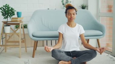 Oldukça karışık yarış kız dizlerinin üzerinde elleriyle lotus pozisyon katta oturan ve meditasyon, rahatlama ve huzur zevk. Yoga, insanlar ve ev kavramı.