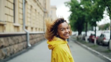 Ağır çekim sokakta yürürken, kameraya dönüm ve gülerek ve gülümseyerek kameraya bakarak Afrikalı-Amerikalı genç portresi. Duygular, şehirler ve insanlar kavramı.