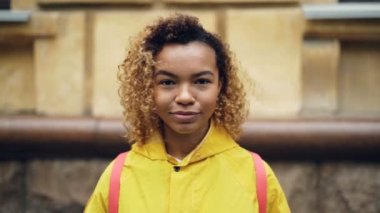 Ağır çekim kameraya bakıyor ve gülümsüyor sonra açık havada duran gülüyor kıvırcık saçlı mutlu Afrikalı-Amerikalı kadın portresi. İnsanlar ve duygular kavramı.