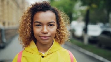Yakın çekim ağır çekim portre çekici karışık yarış kız kameraya mutlu gülümseme açık havada sokağın ortasında duran olumlu duygular ifade ile.