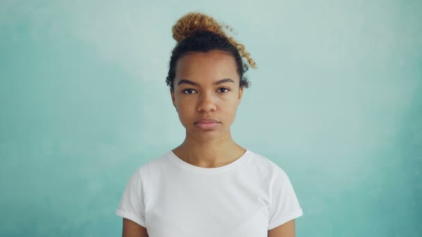 Retrato de una bonita chica afroamericana mirando a la cámara con la cara recta y luego sonriendo y riendo. Emociones humanas, cambio de humor y concepto juvenil . — Vídeos de Stock