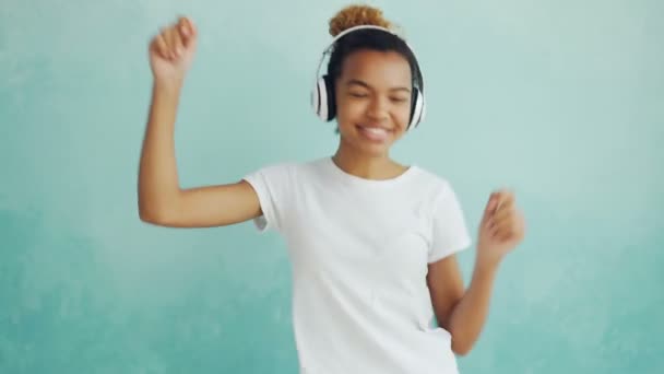 Retrato de una mujer afroamericana feliz escuchando música a través de auriculares inalámbricos y bailando disfrutando de la melodía. Tecnología moderna, gente y concepto divertido . — Vídeo de stock