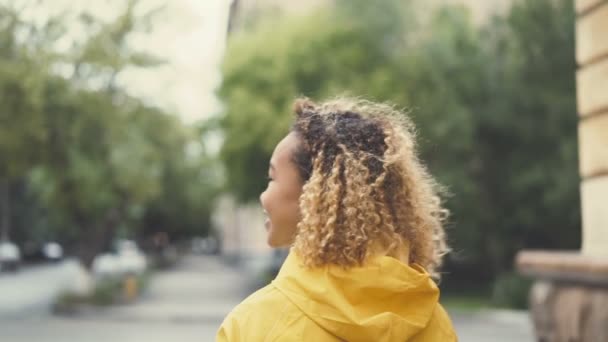 Primer plano retrato en cámara lenta de una mujer afroamericana caminando por la calle, girando y mirando a la cámara con un abrigo brillante. Concepto de personas y estilo de vida urbano . — Vídeos de Stock