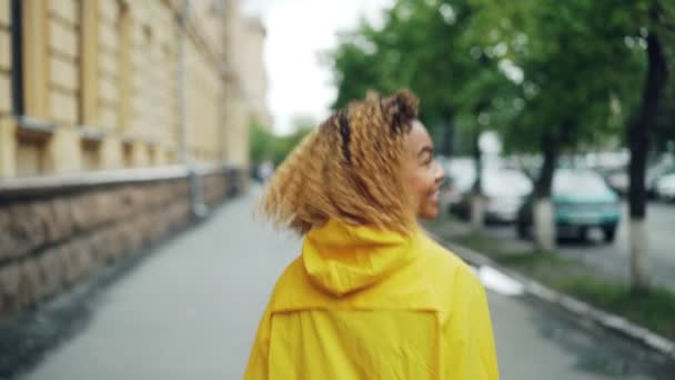 Retrato en cámara lenta de una hermosa joven estudiante afroamericana caminando por la calle, girando y mirando a la cámara con una sonrisa feliz. Concepto de emociones, ciudades y personas . — Vídeos de Stock