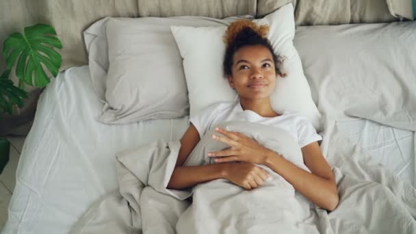 Gelukkig jongedame liegt in bed wakker en lachende genieten van zorgeloos leven, comfortabel bed en goed nieuws. Positieve emoties, bedtijd en jeugd concept. — Stockvideo