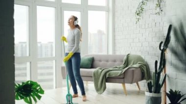 Güzel kız düz plastik paspas ve kulaklık müzik, dans ve güzel bir daire içinde rutin ev işi sırasında şarkı ile zemin yıkama.