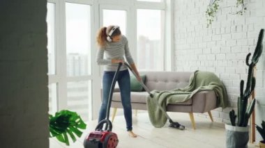 Güzel kadın ev modern elektrikli süpürge kullanarak ve kulaklık ile müzik, dans ve şarkı kat boya. Ev işleri ve teknoloji kavramı.