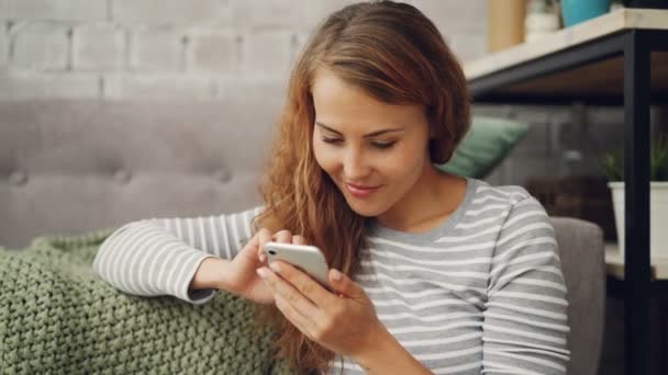 Счастливая молодая женщина держит смартфон трогательным экраном и улыбается, проверяя аккаунт в социальных сетях или читая сообщения. Современные технологии и концепция тысячелетия . — стоковое видео