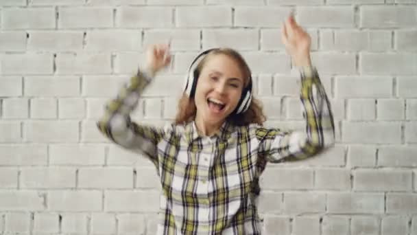 Portret van gelukkig meisje in stijlvolle kleding dansen, zingen en luisteren naar muziek in draadloze hoofdtelefoons. Millennials, moderne elektronica en jongeren concept. — Stockvideo