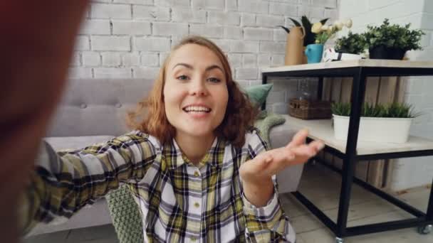Portrait de jeune femme heureuse regardant la caméra, tenant gadget et parlant à des amis en ligne souriant et gesticulant debout à la maison. Communication et concept de personnes . — Video