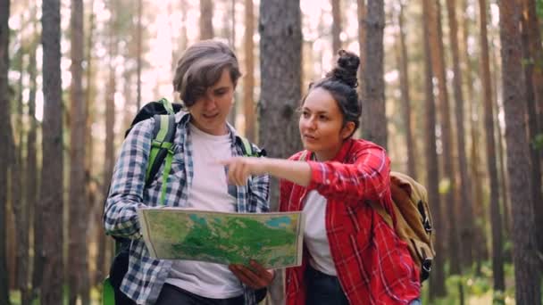 Los turistas perdidos están de pie en el bosque mirando el mapa, hablando y haciendo gestos y luego encontrando el camino y caminando al lugar de destino. Concepto de personas, viajes y naturaleza . — Vídeos de Stock