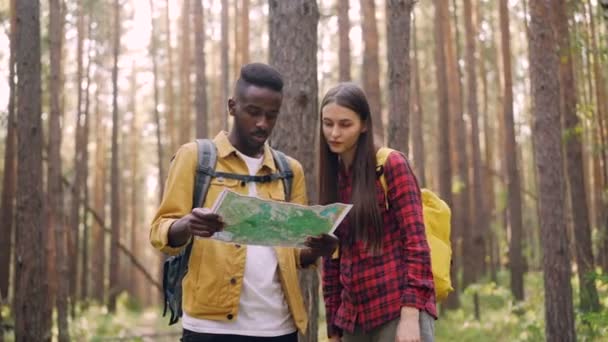 Dois amigos estão olhando para o mapa na floresta, apontando na mesma direção, rindo e caminhando juntos. Estilo de vida ativo, amizade e conceito de juventude . — Vídeo de Stock