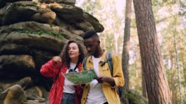 Mutlu esmer kıvırcık saçlı arıyor kayalar yakınındaki ormanda erkek arkadaşı haritaya, arıyor iken ayakta dürbün ile insanlar konuşuyor.