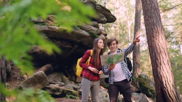 Les voyageurs joyeux regardent la carte debout dans le bois près des rochers discuter chemin et regarder autour à travers des jumelles puis marcher dans la direction choisie . — Video